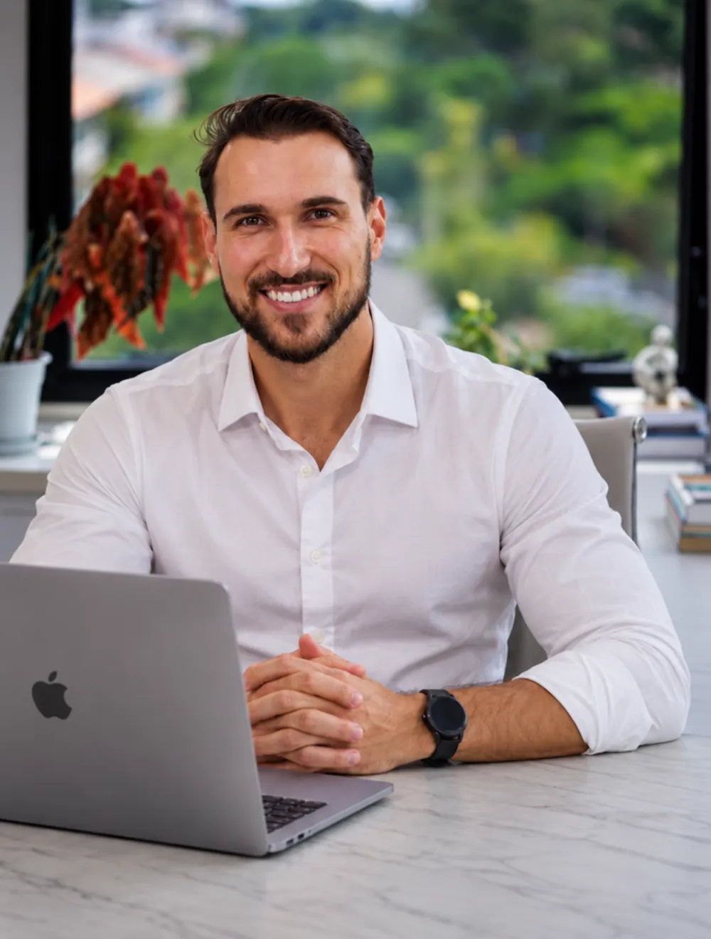 João Guilherme sorrindo, de camisa branca, sentado à mesa com o notebook