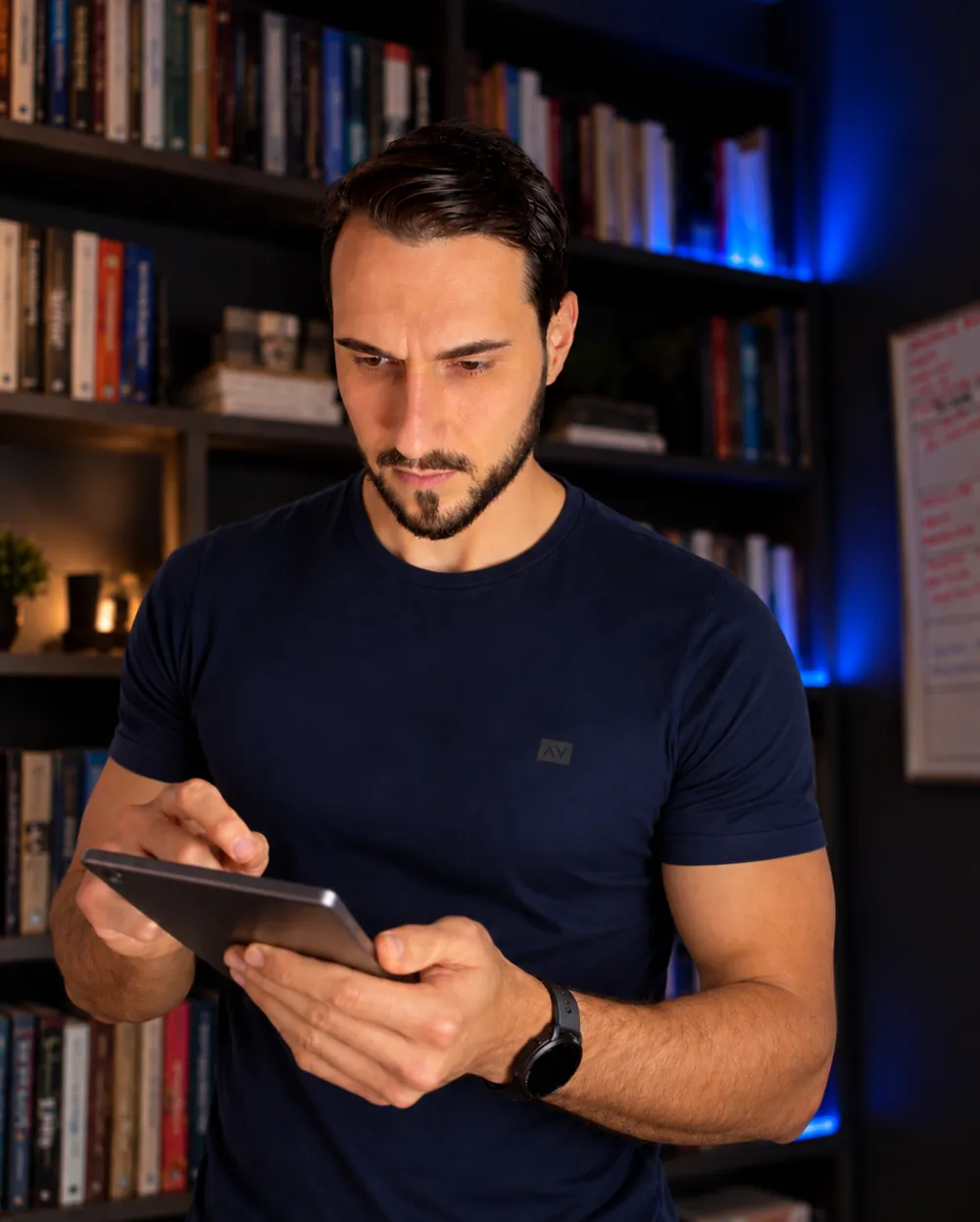 João Guilherme analisando dados em um tablet, com uma estante de livros ao fundo